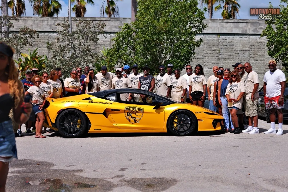 Rally participants in matching Motivation Rally shirts lined up behind a yellow Lamborghini wrapped with the rally crest